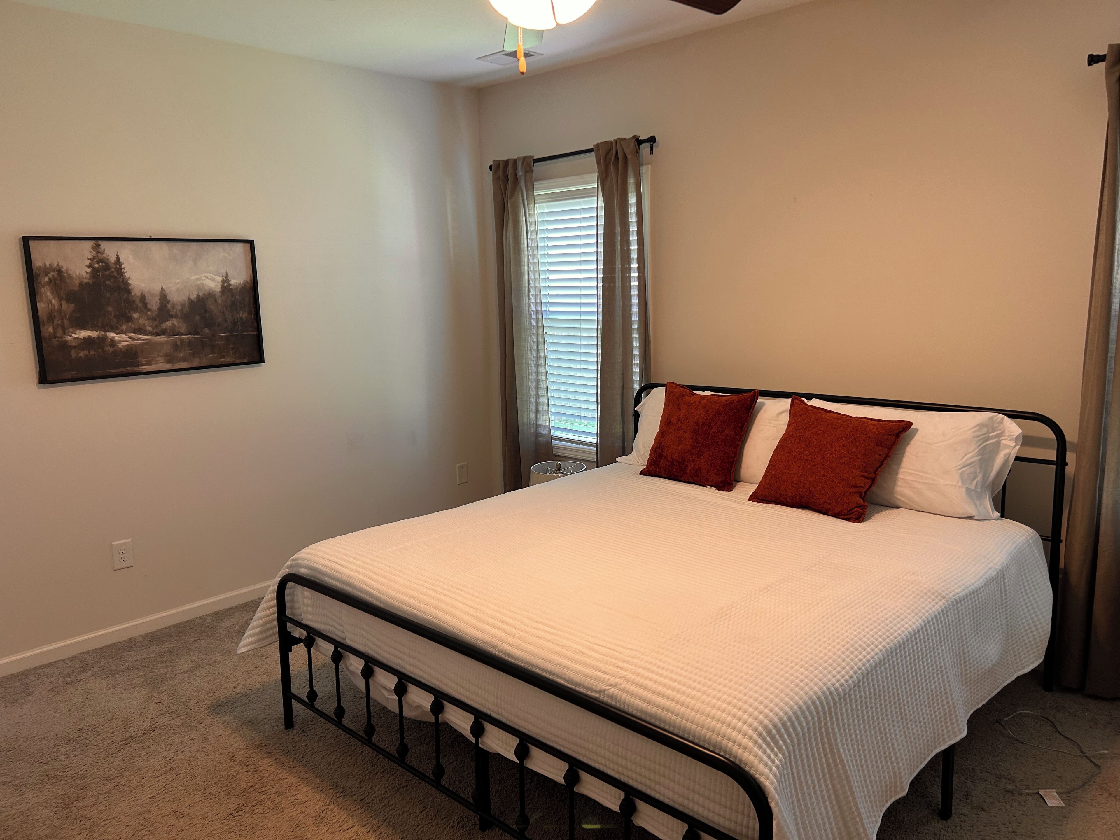 A bedroom with a bed, a painting on the wall, and a window with curtains.