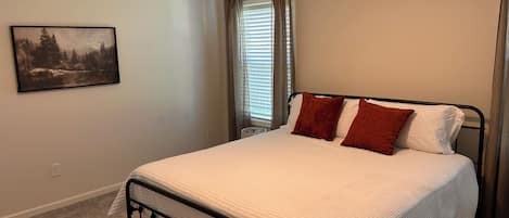 A bedroom with a bed, a painting on the wall, and a window with curtains.