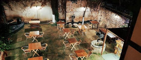 An outdoor seating area with tables and chairs, surrounded by stone walls and trees.