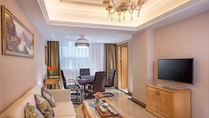 Habitació d'hotel amb un sofà, una taula de menjador amb cadires, una televisió i una làmpada penjant.