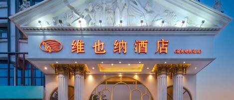 A hotel entrance with a classical facade, columns, and a large illuminated sign.