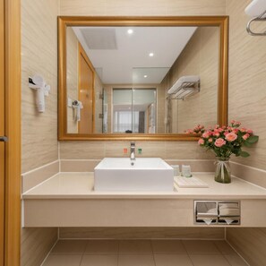 A bathroom with a large mirror, a white sink, and a vase of flowers. - Vienna Hotel Shenzhen (Shenzhen)