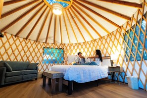 A yurt interior with a bed, a sofa, a table, and a window.