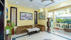 A hotel lobby with a sofa, a coffee table, decorative panels, framed artwork, and a large vase. - Le Pavillon Villa (Da Nang Municipality)