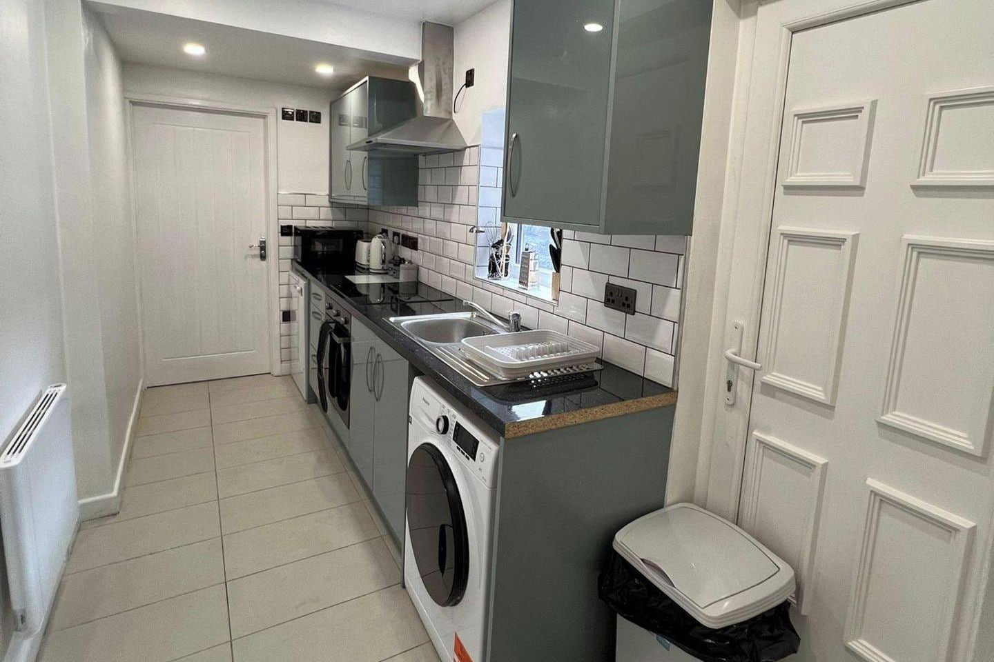 A compact kitchen with a washing machine, a sink, and a trash bin.