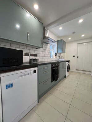 A modern kitchen with grey cabinets, a dishwasher, a washing machine, and a countertop with various kitchen items. - Florence House Sleeps 13 - Free Parking & Garden (West Bromwich)