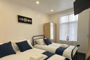 Een hotelkamer met twee bedden, een kledingkast, een raam met gordijnen en een kunstwerk aan de muur.
