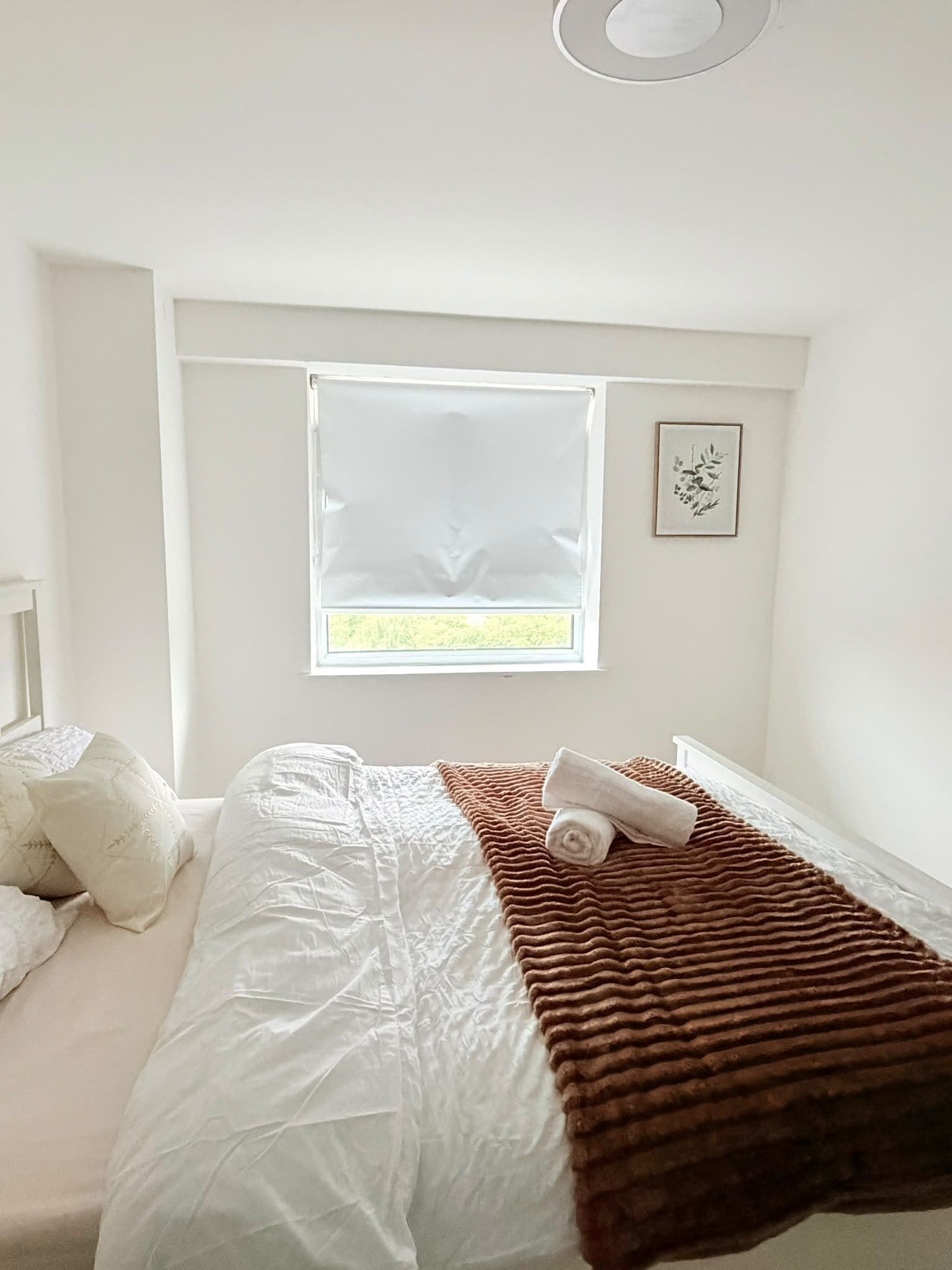 Een slaapkamer met een bed, een raam en een aan de muur hangend schilderij.