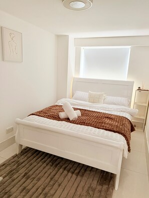 Ein Schlafzimmer mit einem weißen Bett, einer braunen Decke und einem braunen Teppich.