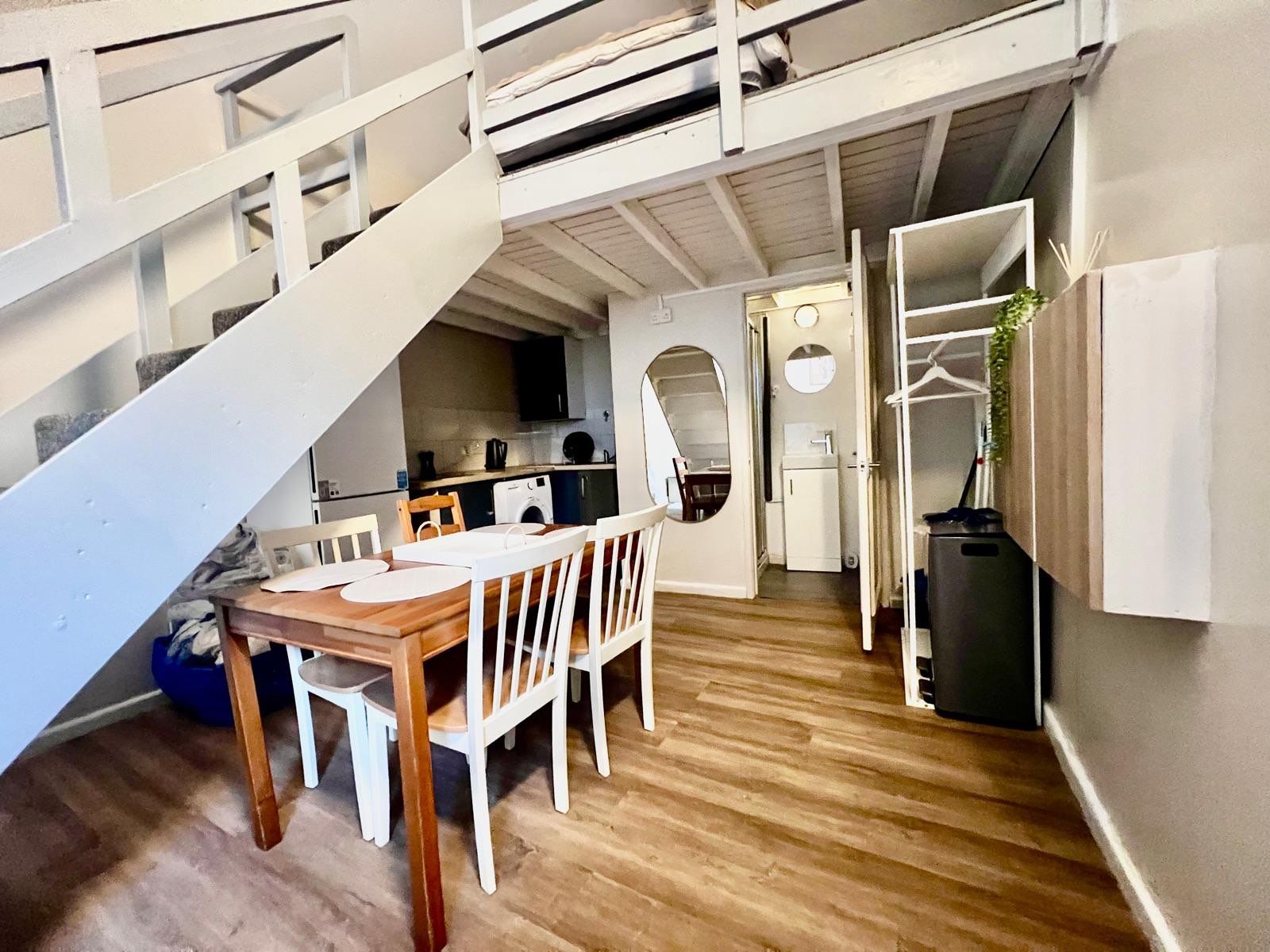 A compact living space with a dining area, kitchen, and a staircase leading to an upper level.
