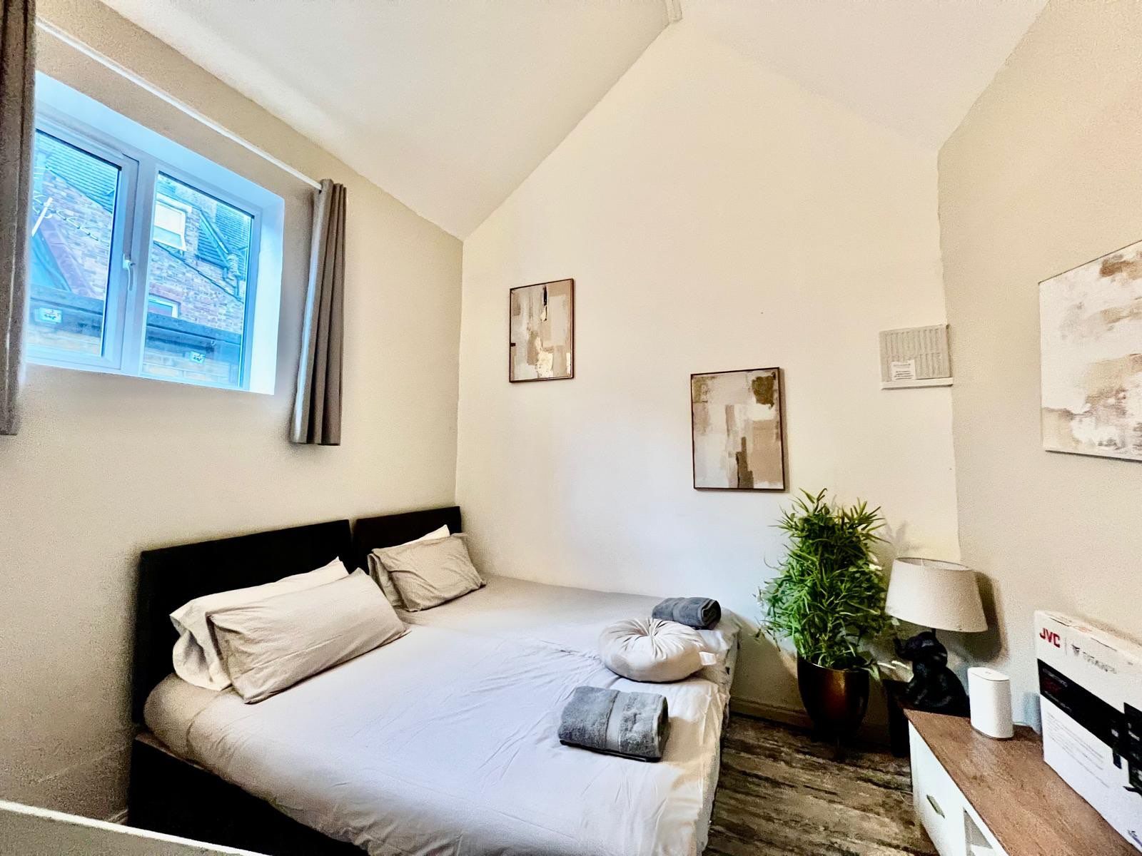 Een slaapkamer met een bed, een raam, een plant en kunstwerken aan de muren.