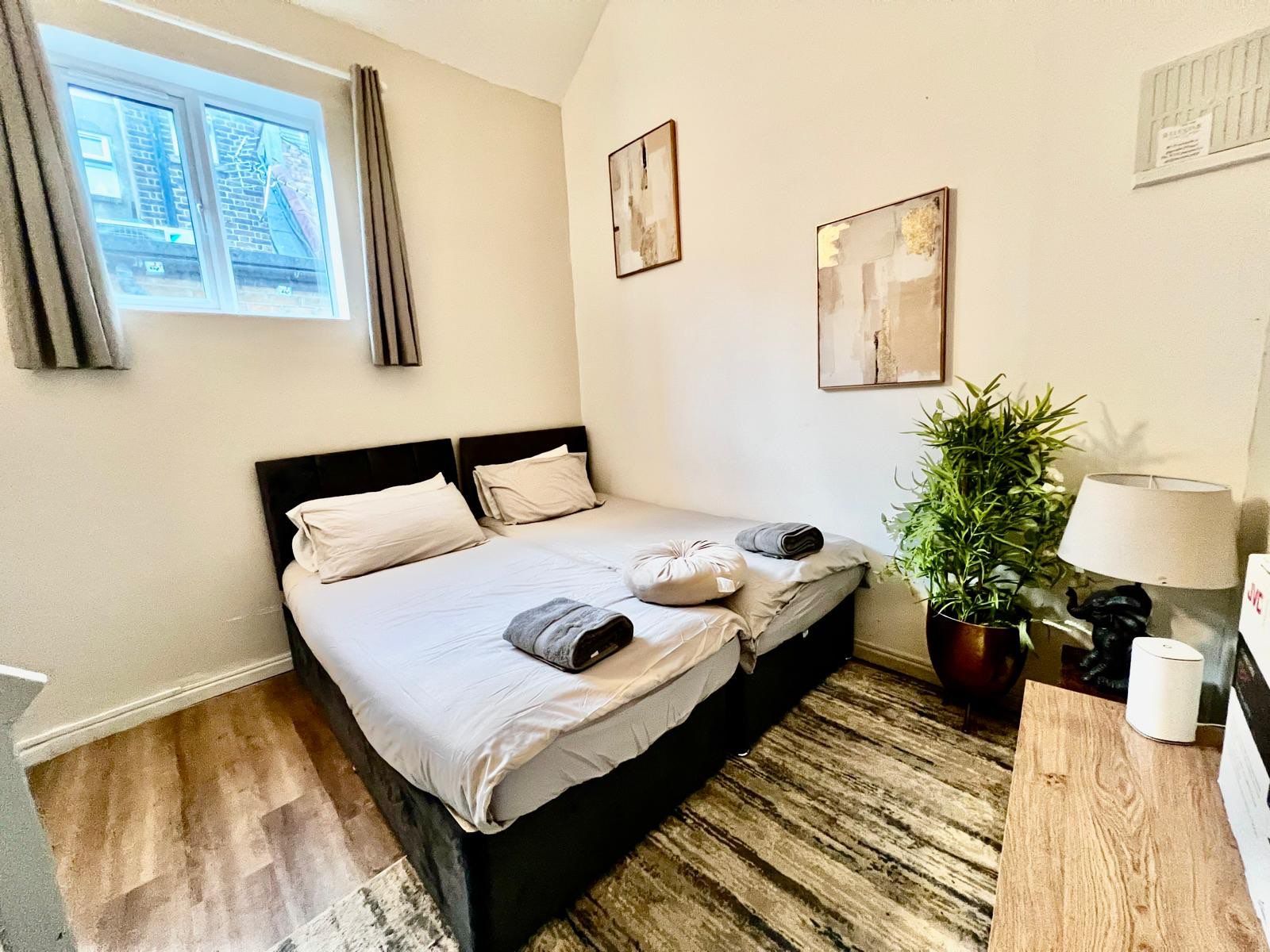 A bedroom with a bed, a potted plant, a lamp, and artwork on the wall.