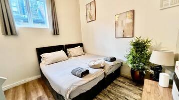 A bedroom with a bed, a potted plant, a lamp, and artwork on the wall.