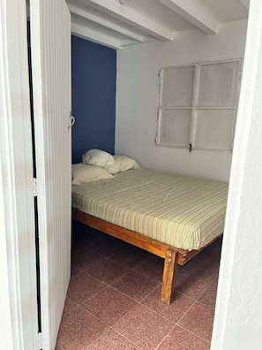 Ein Einzelbett mit Holzrahmen und einer gestreiften Matratze in einem Zimmer mit blauer Akzentwand und einer weißen Tür.
