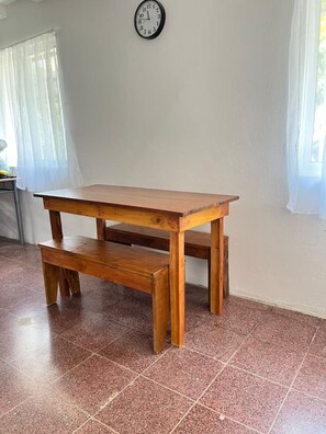 Ein Holztisch mit einer Bank in einem Raum mit Fliesenboden und einer Uhr an der Wand.