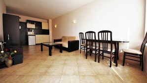 Un espacio de estar con un sofá, una mesa de centro y una mesa de comedor con sillas. Incluye una cocina con alacenas y un refrigerador.