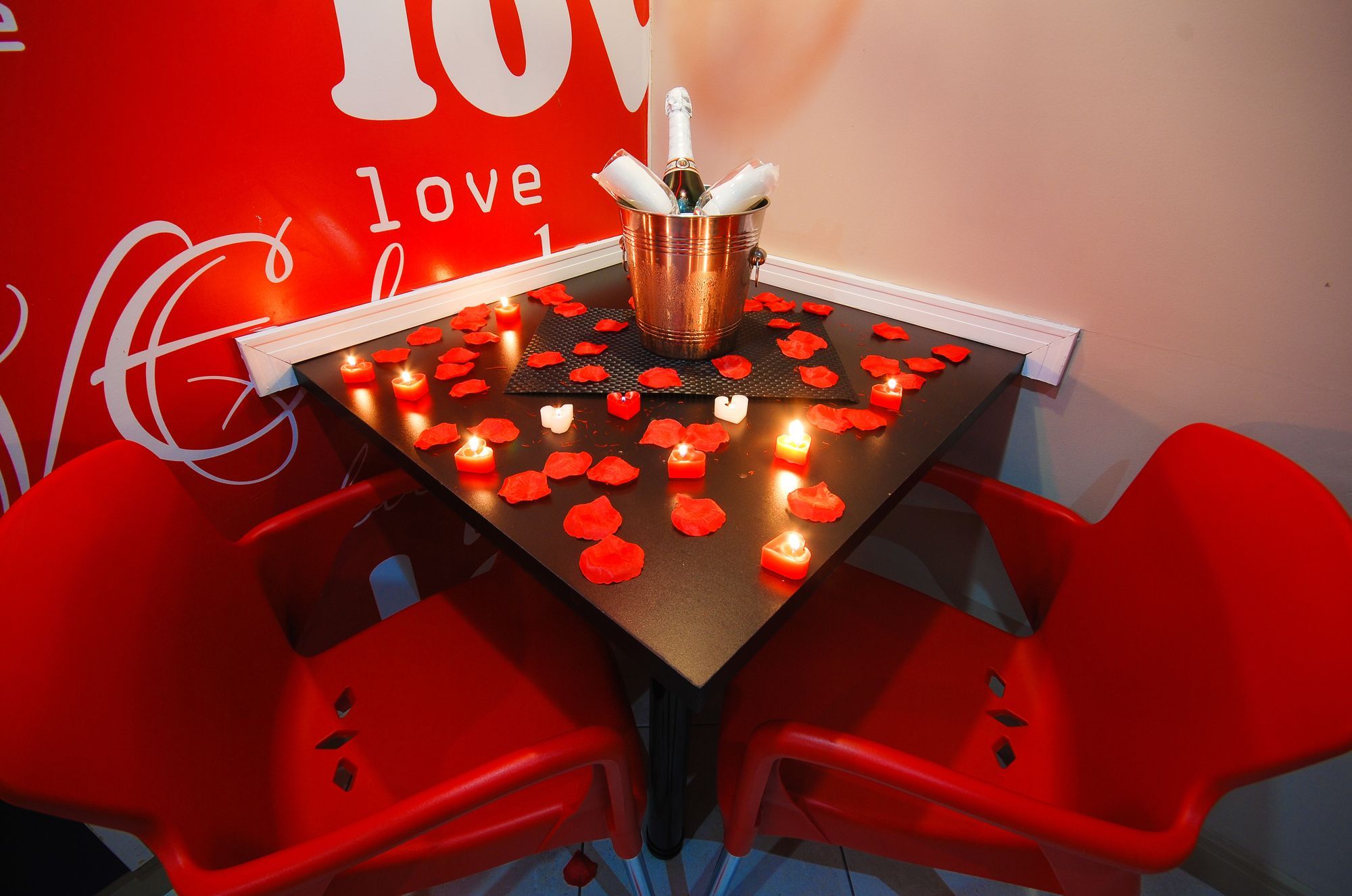 Uma mesa com garrafa de champanhe, velas e pétalas de rosa.