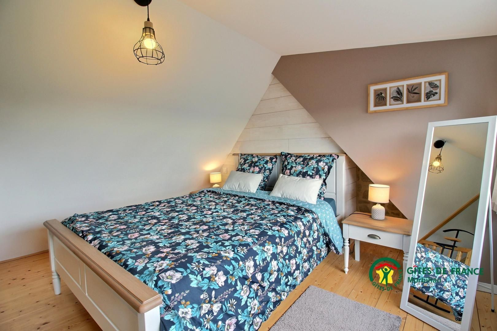 Een slaapkamer met een bed, nachtlampjes, een spiegel en een lijst met een afbeelding aan de muur.