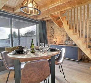 Ein Essbereich mit einem runden Tisch, Stühlen und einer Weinflasche. Im Hintergrund ist eine Treppe mit Holzwangen zu sehen.