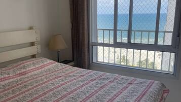 A bedroom with a bed, a window with a view of the sea, and a lamp.