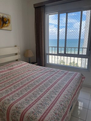 Een slaapkamer met een bed, een raam met uitzicht op zee en een lamp.