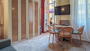 A hotel room with a dining area, a TV mounted on the wall, and a view through a large window. - Hôtel Au Picardy (Nice)