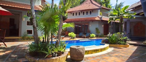 A courtyard with a swimming pool, palm trees, and a building with a tiled roof.