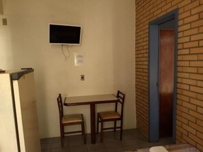 Ein kleines Zimmer mit einem Tisch und zwei Stühlen, einem an der Wand befestigten Fernseher und einer Tür mit blauem Rahmen.