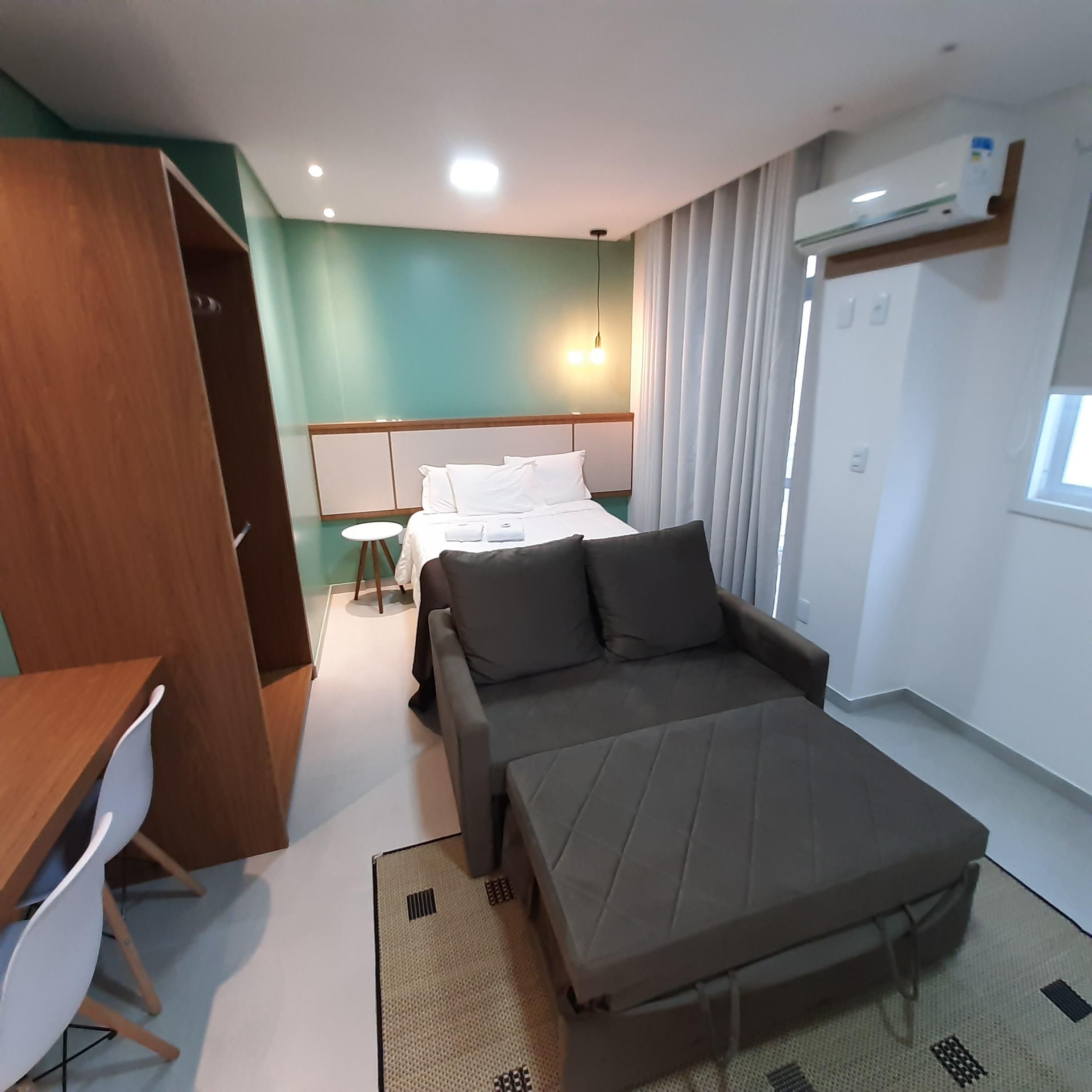 Et hotelværelse med seng, sofa, skrivebord og garderobeskab.