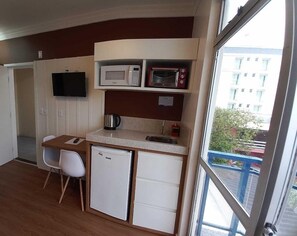 A compact kitchenette with a microwave, toaster, and coffee maker. There is a small refrigerator and a dining area with a chair. - Residencial Pousada Do Mar Azul (Florianópolis)