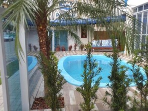 An indoor swimming pool with a tiled deck, surrounded by potted plants and a palm tree. - Residencial Pousada Do Mar Azul (Florianópolis)