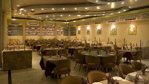A restaurant with multiple dining tables and chairs, decorative wall art, and a ceiling with recessed lighting. - L M B Hotel (Jaipur)
