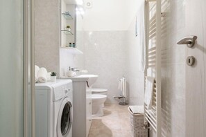 A compact bathroom with a washing machine, toilet, and a towel rack. - House Zamboni 12 (Bologna)