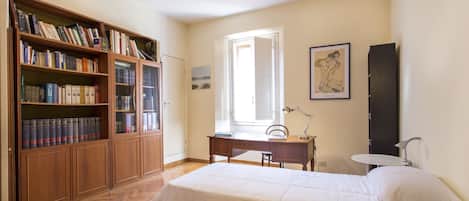 A bedroom with a bed, a desk, a chair, a bookshelf, and a window.
