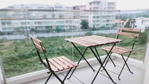 Un balcó amb dues cadires de fusta i una taula, amb vista a una zona residencial amb diversos edificis.