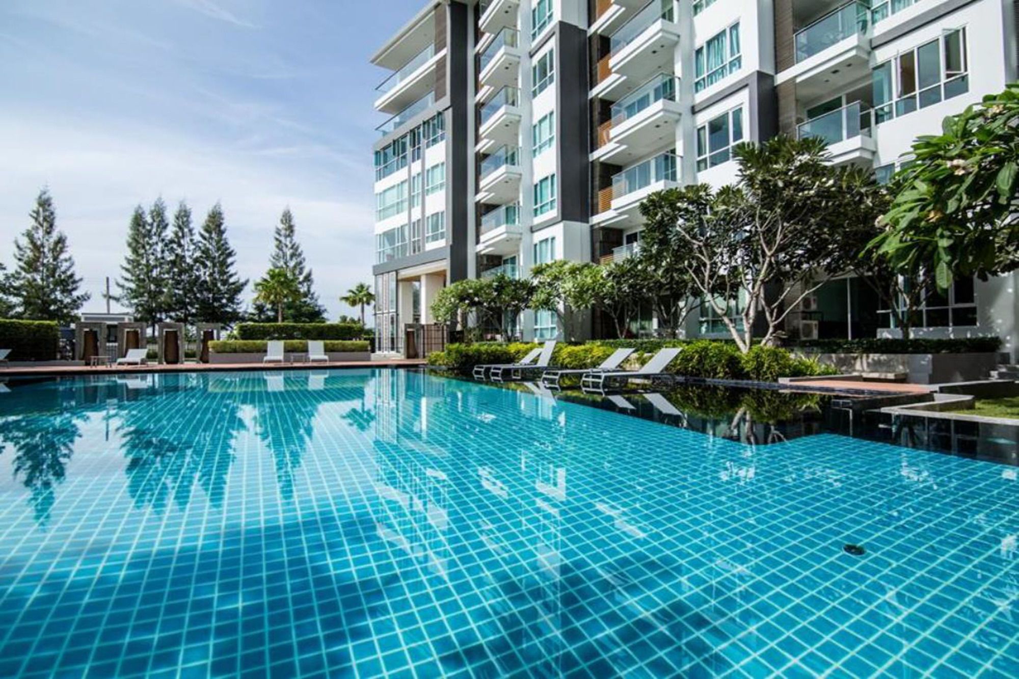 Un hotel moderno con piscina, diversi balconi e vegetazione lussureggiante.