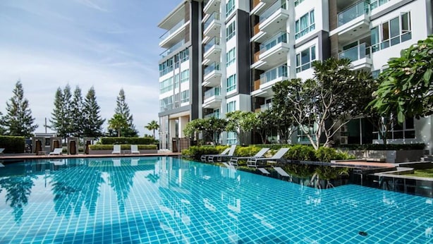Una piscina amb superfície de rajola, envoltada per un edifici modern amb múltiples balcons i un cel serè.