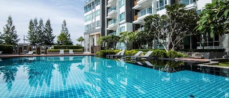 A modern hotel with a swimming pool, multiple balconies, and lush greenery.