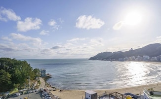Vista costera con playa, zona de estacionamiento y un edificio de techo plano.