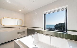 Un baño moderno con una bañera grande, un tocador con espejo y una ventana con vista al mar.