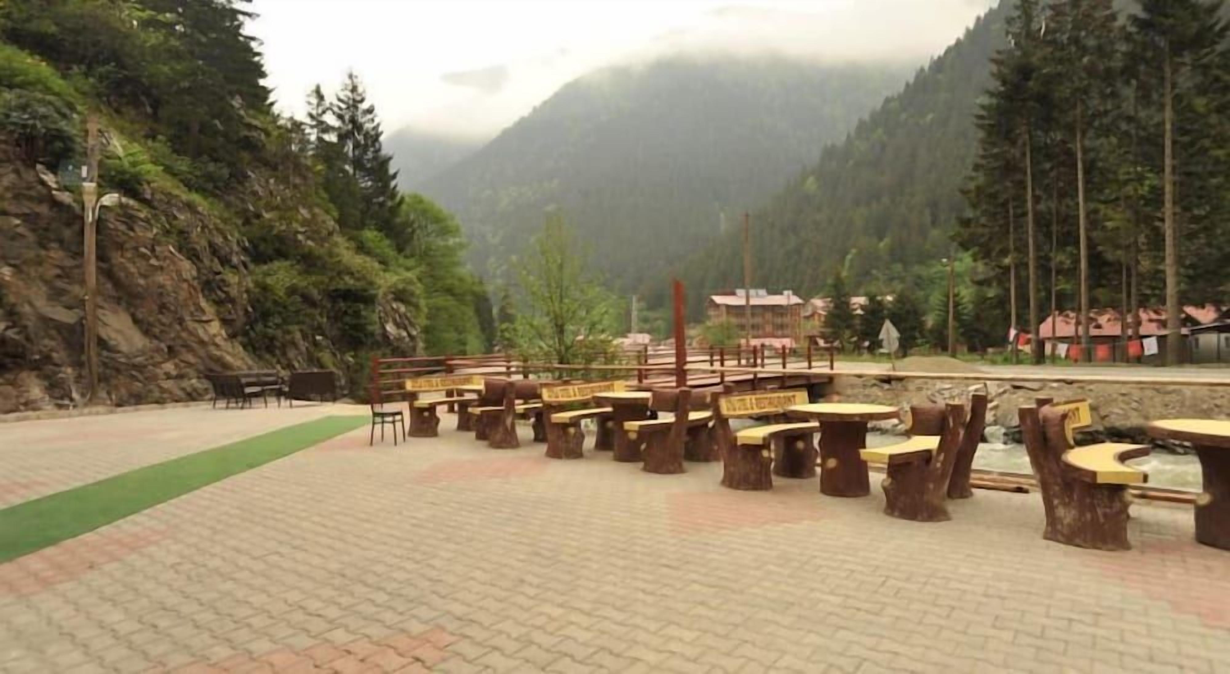 Outdoor seating with benches and tables, a paved area, and a mountainous backdrop.