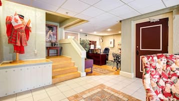 A hotel lobby with a reception desk, a staircase, a floral sofa, and a mannequin in a red uniform.