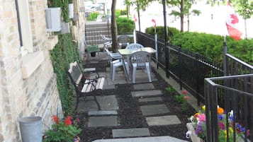 A paved outdoor seating area with tables and chairs, a trash can, and potted plants.