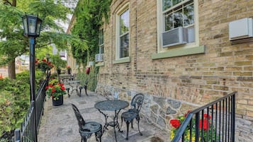 An outdoor patio with stone flooring, metal tables, and chairs, surrounded by brick walls and greenery.