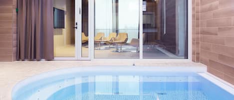 Piscina com chão de azulejos, porta de vidro e cadeiras amarelas dentro de um espaço com paredes revestidas.