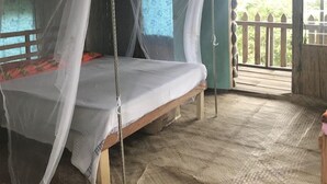 Ein Zimmer mit einem Bett unter einem Moskitonetz, Holzboden und Blick ins Freie.