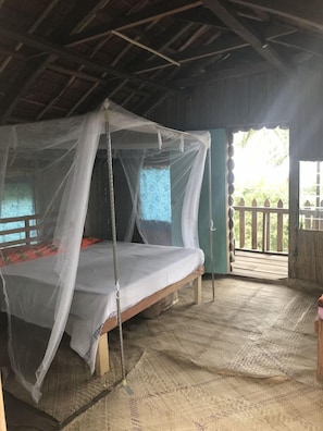 A room with a bed under a mosquito net, a wooden floor, and a view of the outside. - Tanna Lava View Bungalows (Tanna Island)