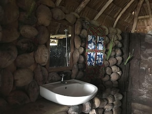 A rustic bathroom with a stone wall, a white sink, and a mirror. - Tanna Lava View Bungalows (Tanna Island)