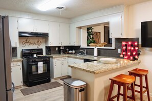 A kitchen with white cabinets, a black stove, a sink, a trash can, and a bar stool. - Spacious 4-bedroom house in Historic College Station near TAMU (College Station)