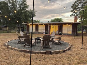 A wooden cabin with a circular seating area surrounded by gravel, featuring Adirondack chairs and a small table. - Spacious 4-bedroom house in Historic College Station near TAMU (College Station)